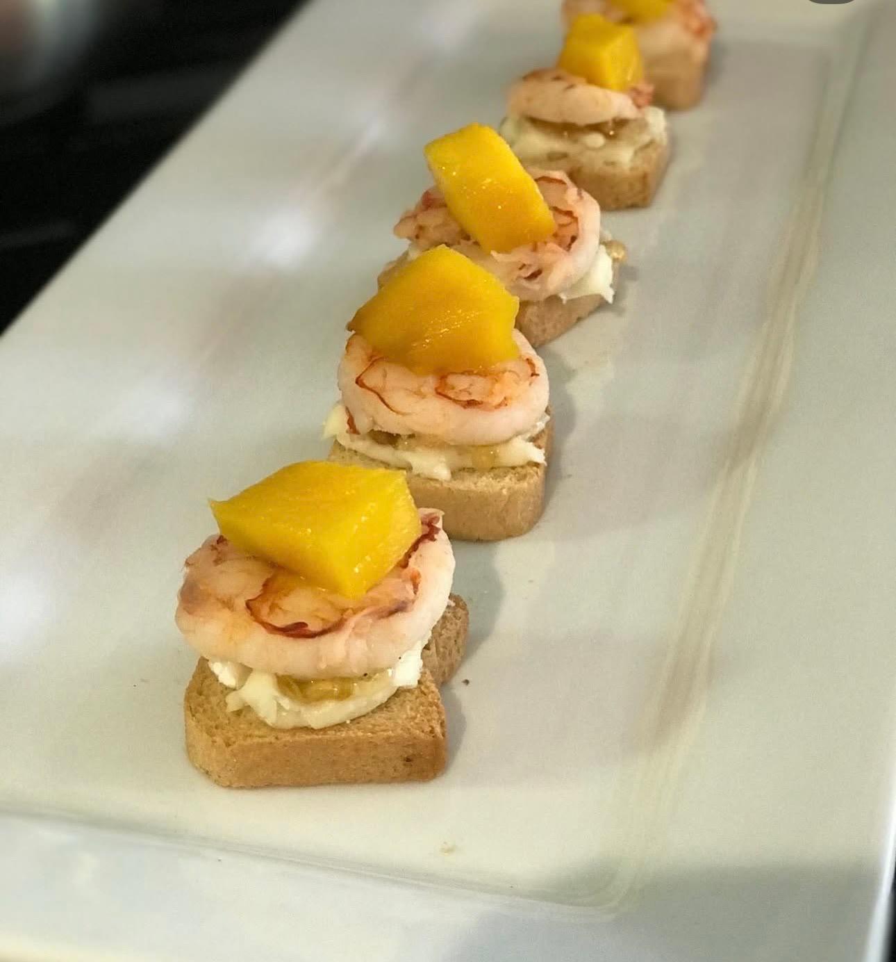 Shrimp canapés topped with diced fruit, lined up on a white platter